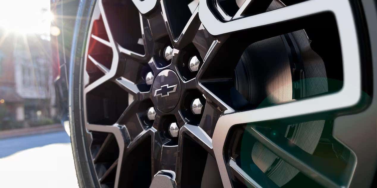 Close-up of a black and silver wheel of a vehicle with a sunburst effect in the background. The wheel features a Chevrolet logo at the center, and the image presents a detailed view of the wheels stylish design.