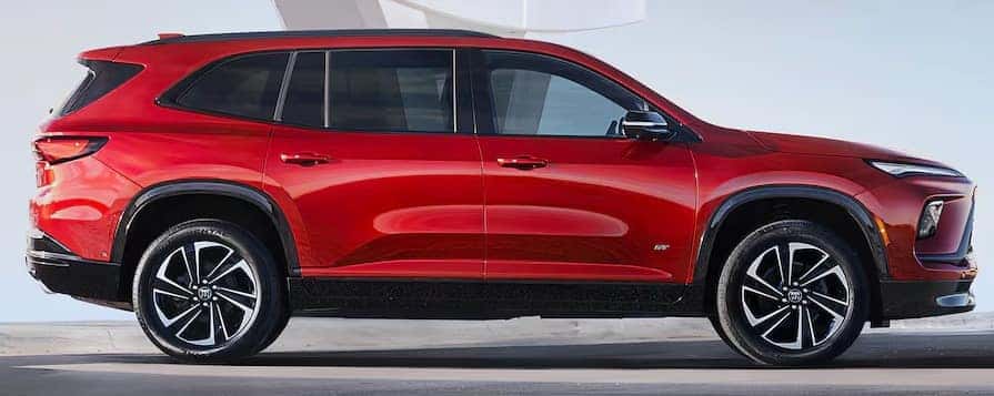 Side view of a sleek, red SUV with a modern design, black tinted windows, and silver alloy wheels. The vehicle is parked on a smooth surface with a clear sky in the background.