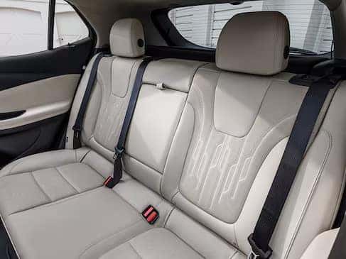 The image shows the back seat of a car with light beige leather upholstery. There are three headrests and three seat belts, with a clean, modern interior design.
