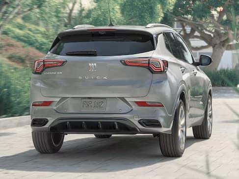 A silver SUV is parked outdoors on a paved surface. The vehicle is seen from the rear, showing its taillights and license plate area. Trees and greenery are visible in the background, creating a natural setting.
