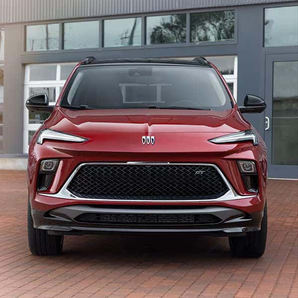 Red modern SUV parked on a brick driveway in front of a building with large windows. The car features sleek lines, a black grille, chrome accents, and LED headlights, conveying a sporty appearance.