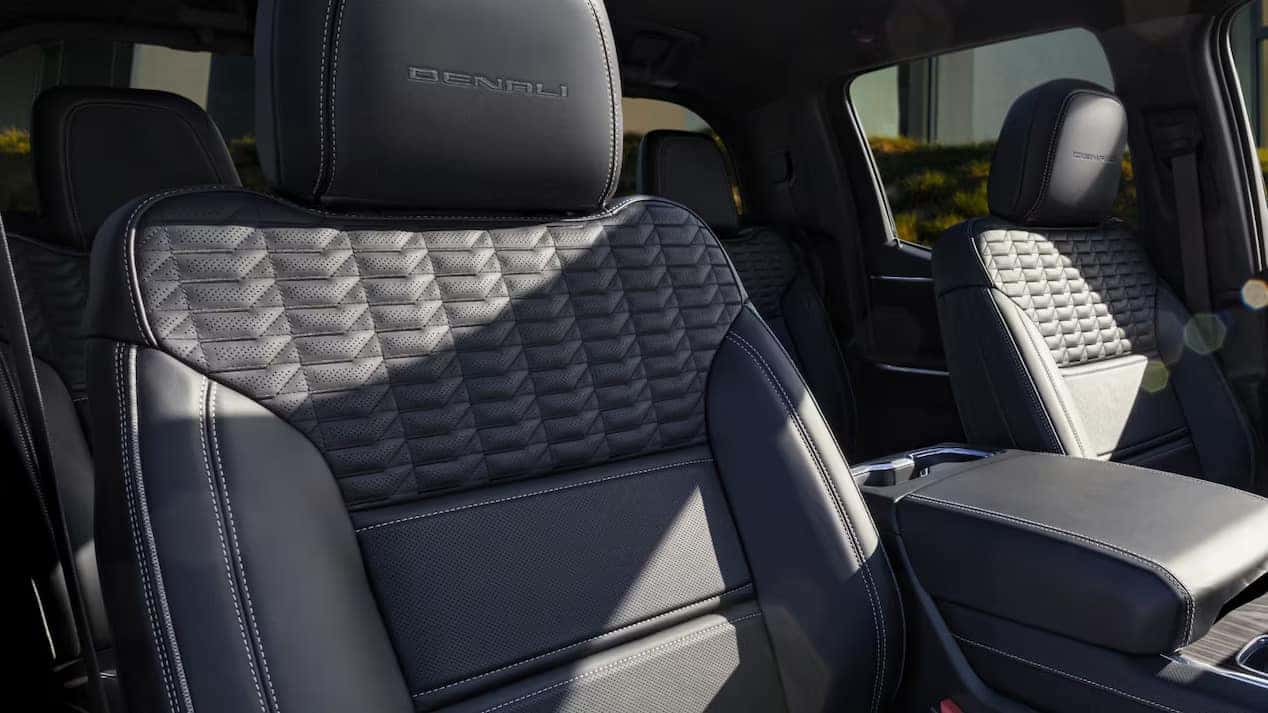 Interior of a vehicle showcasing black leather seats with diamond stitching and Denali embroidered on the headrests. The console and armrest are visible, emphasizing a luxurious and modern design. Sunlight enters through the windows.