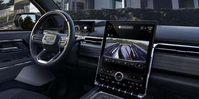 Car interior featuring a steering wheel and a large vertical digital screen on the dashboard displaying a rearview camera image. The interior is sleek with modern design elements, showcasing a high-tech and luxurious feel.
