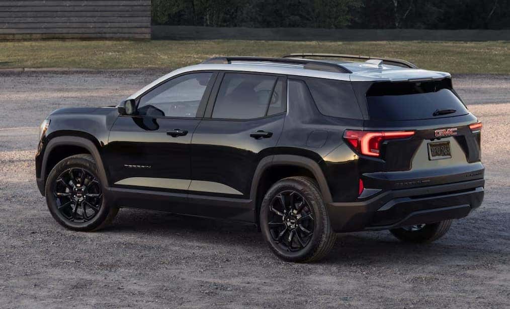 A black SUV is parked on a gravel surface. It features dark-tinted windows, black alloy wheels, and a sleek, modern design. The rear of the vehicle is visible, showcasing red tail lights and a branded logo on the back.