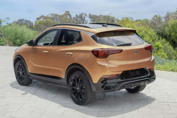 A bronze-colored SUV is parked on a stone-paved driveway with a scenic view of greenery and a clear sky in the background. The vehicle features sleek design elements and black alloy wheels.