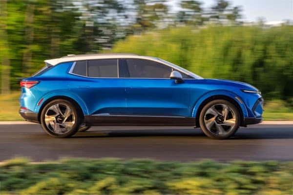 A bright blue SUV is driving on a smooth road, surrounded by blurred greenery. The vehicle has a sleek design with a white roof, and the photo captures the motion of the car.