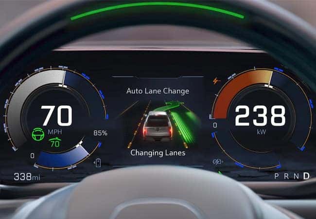 Close-up of a cars digital dashboard displaying speed at 70 MPH and power usage at 238 kW. The center shows a vehicle graphic with Auto Lane Change and Changing Lanes text. Indicators show driving mode and mileage at 338 miles.