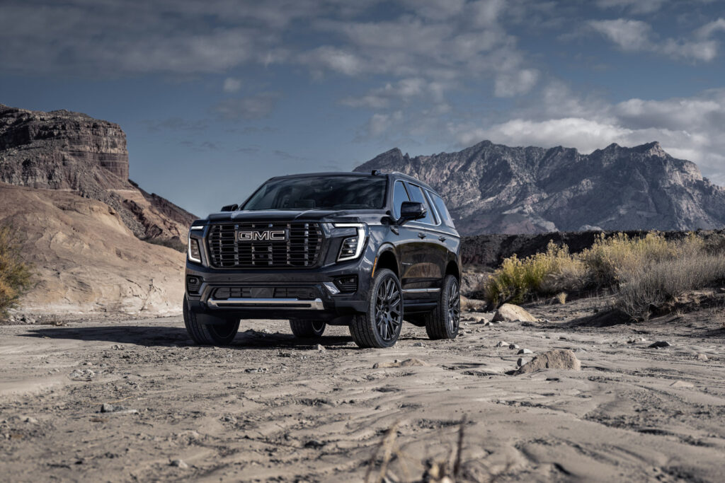 GMC SUV on rocky desert terrain with mountains and blue sky in the background.