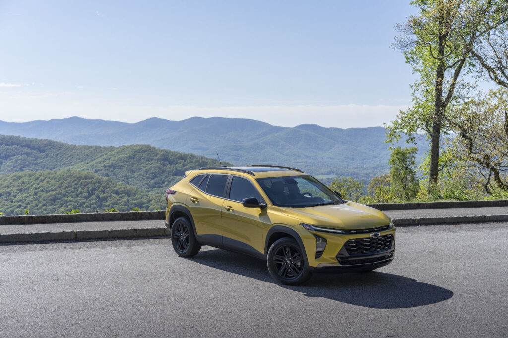 Yellow SUV parked on a mountain overlook, surrounded by lush greenery and distant hills.