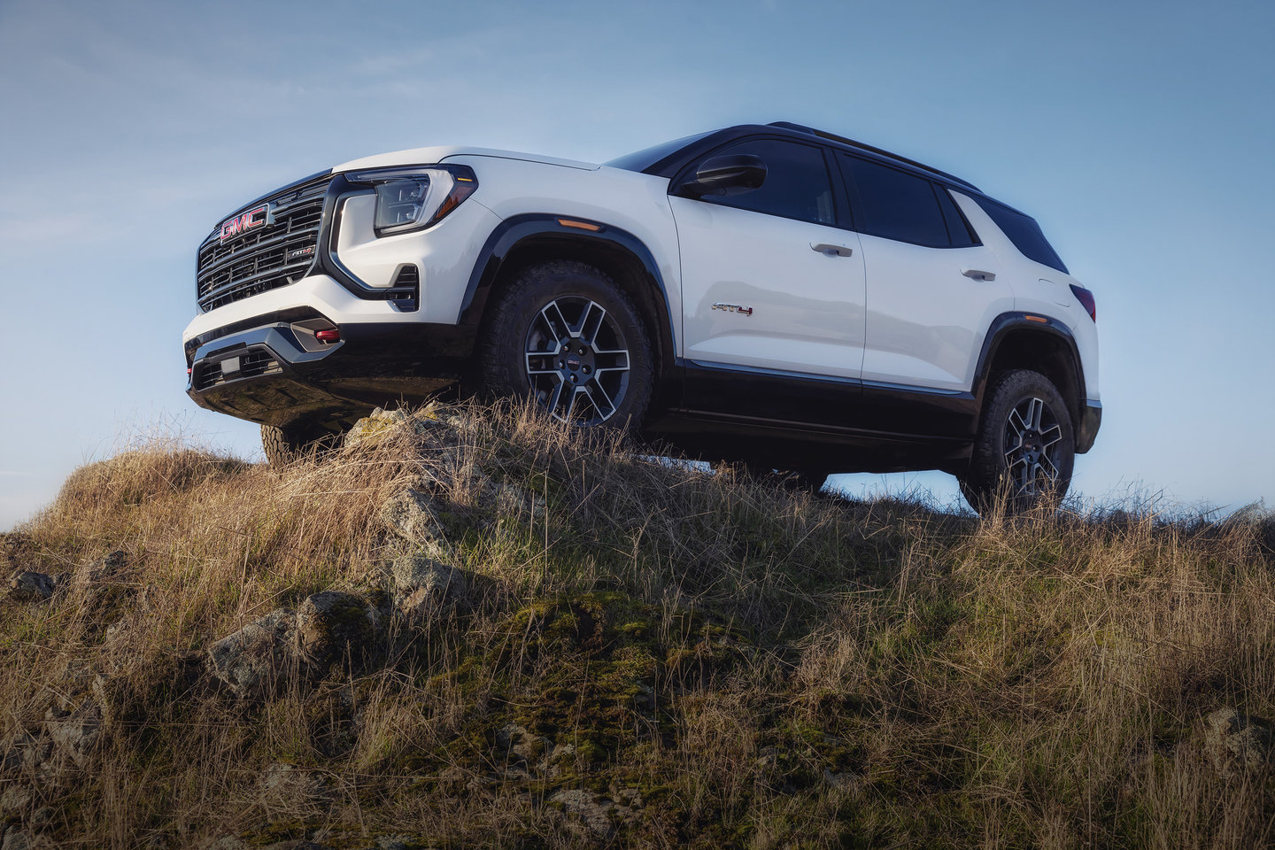 White GMC SUV on a grassy hilltop under a clear blue sky, showcasing off-road capability.