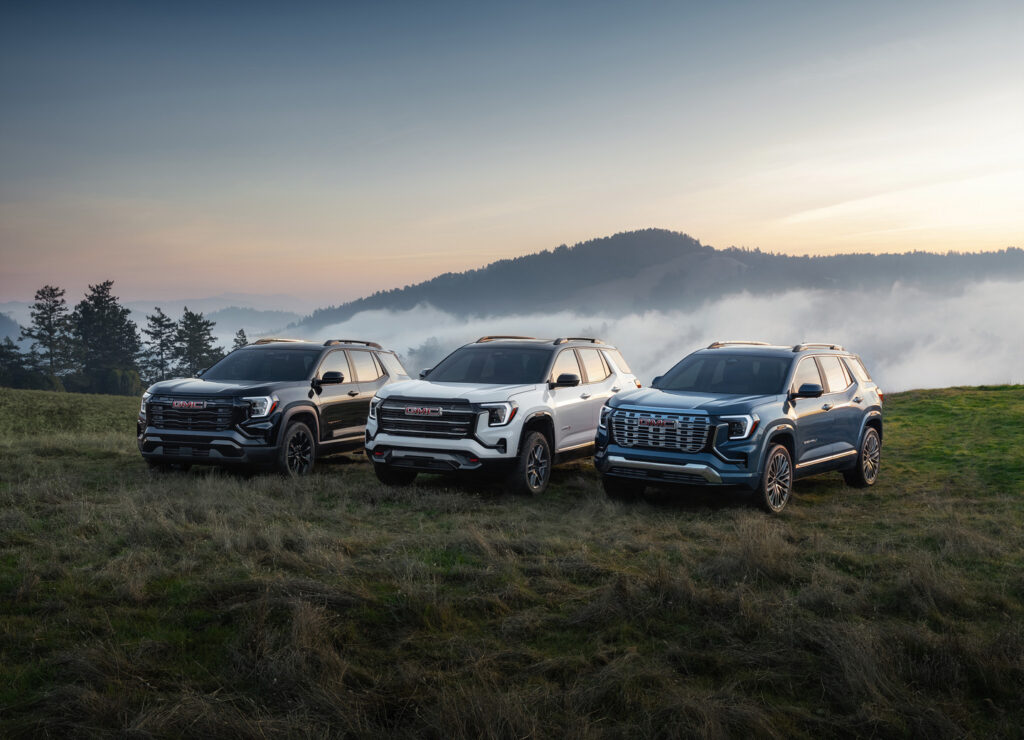 Three SUVs parked on a grassy hill at sunrise, with a misty forested background.