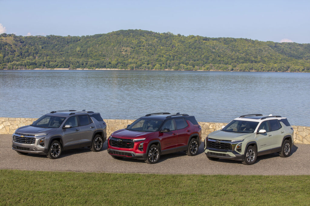 Three SUVs in varied colors parked by a lakeside, with lush hills in the background.