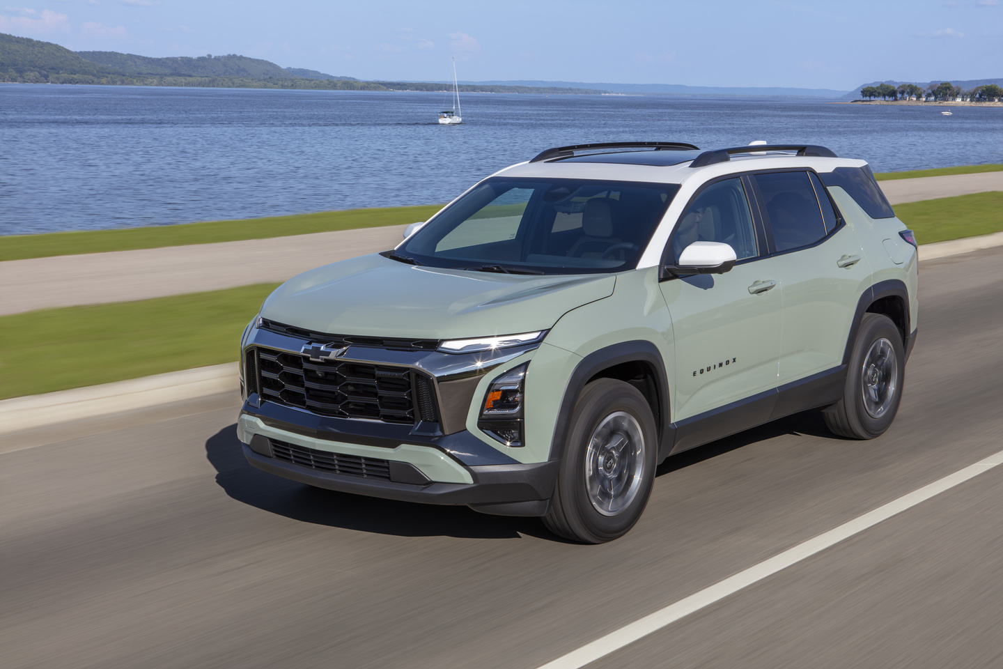 SUV driving on a coastal road with a scenic view of a lake and distant hills.