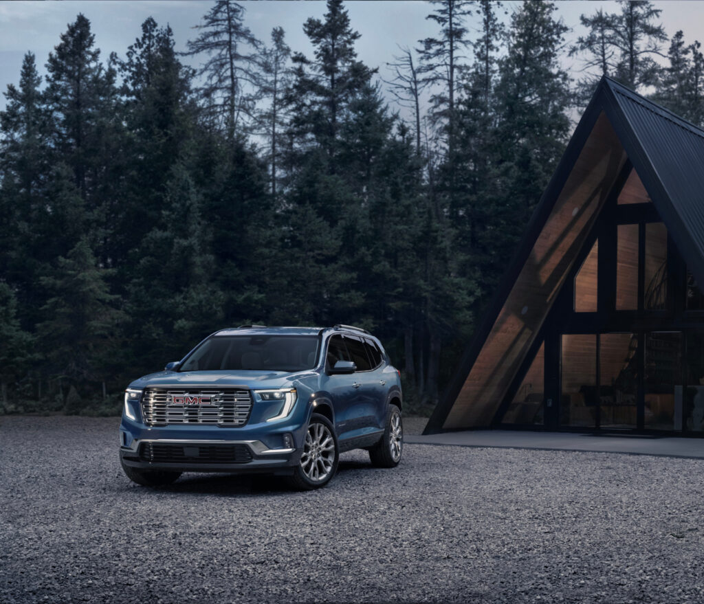 Sleek blue SUV parked near a modern A-frame cabin surrounded by a forested landscape.