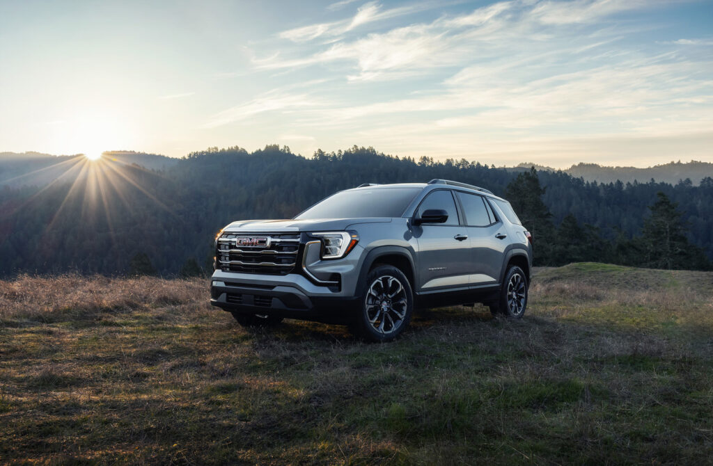 SUV on a grassy hill with a forest and sunrise backdrop, showcasing rugged design.