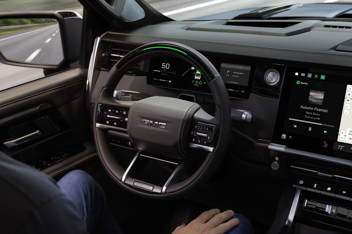 The image shows the interior of a modern car, featuring a steering wheel, a digital dashboard, and a large touchscreen display on the center console. The display shows various controls and settings. The car has a sleek, black design.