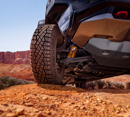 Off-road vehicle's tire and suspension navigating a rocky desert terrain.