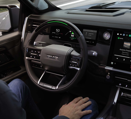 Modern car interior with digital dashboard, touchscreen displays, and a person holding the steering wheel.