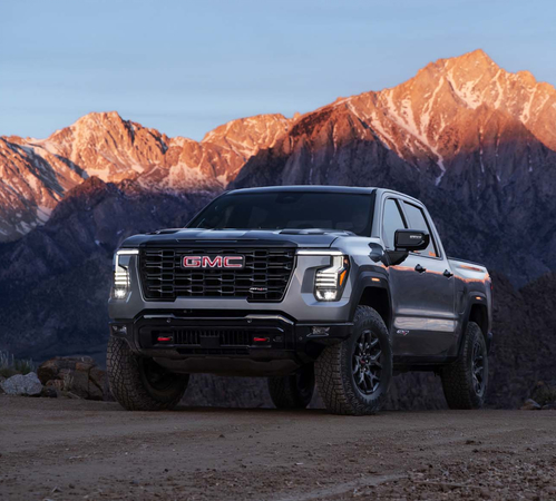 Pickup truck parked on a dirt road against a backdrop of sunlit rocky mountains at dusk.