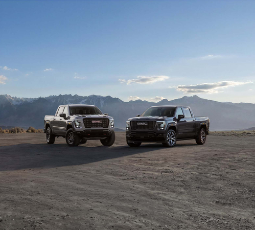 Two GMC pickup trucks parked in a desert landscape with mountain backdrop and clear sky.