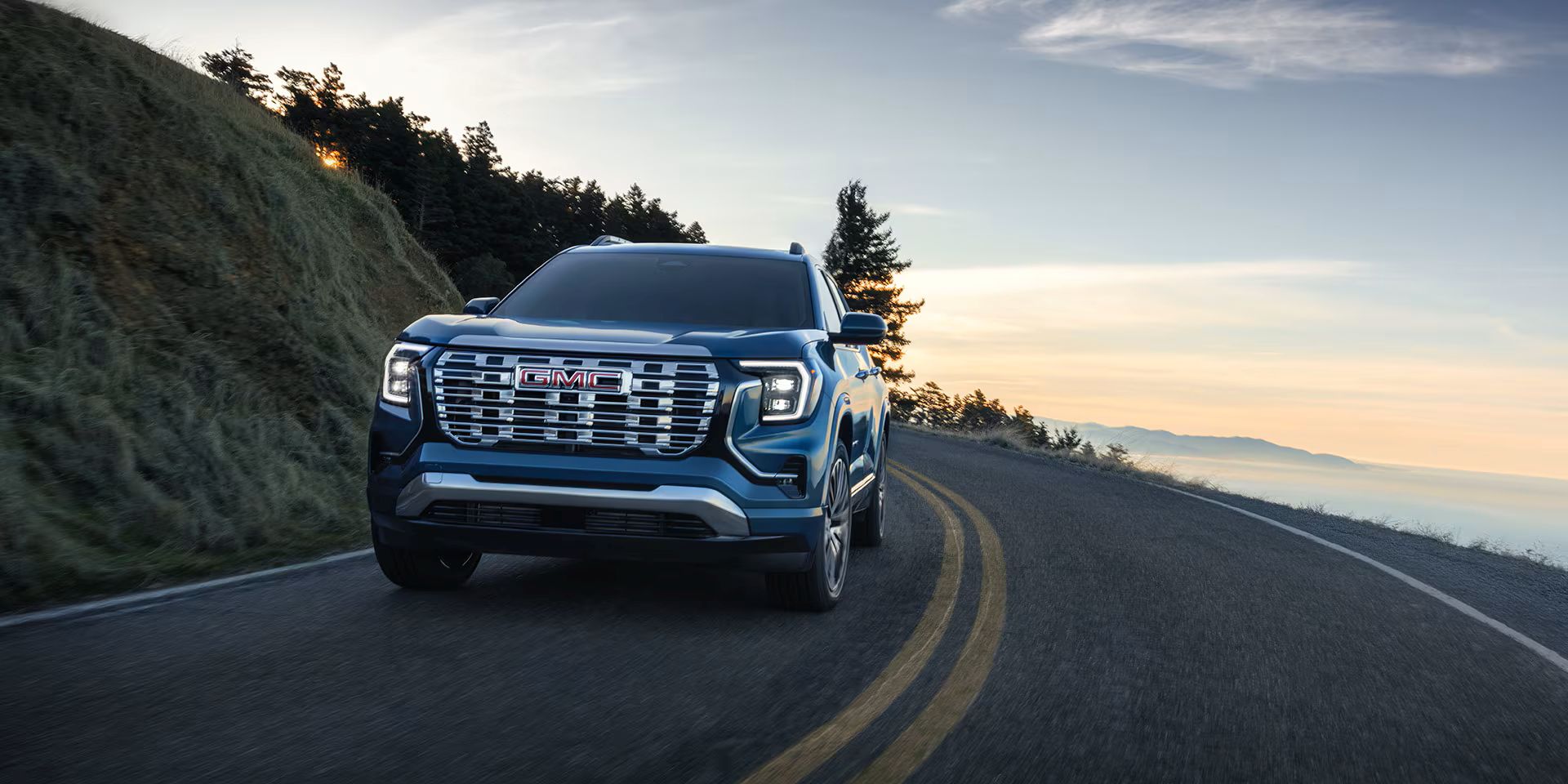 SUV driving on a scenic mountain road at sunset with hills in the background.