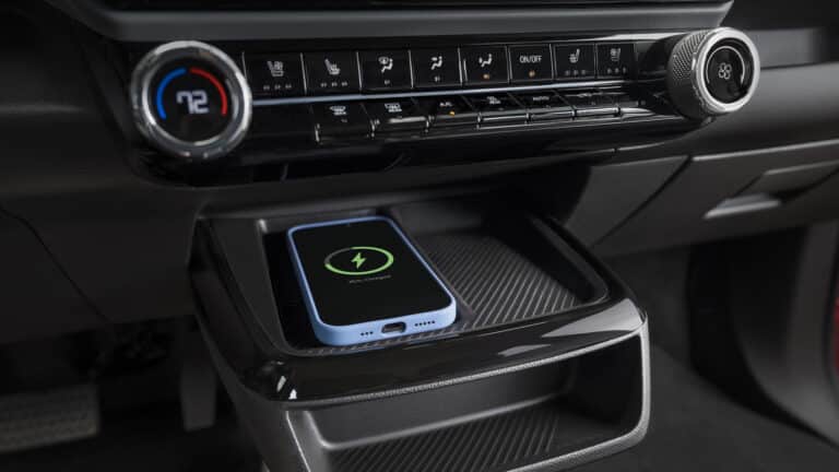 Smartphone wirelessly charging on a car's built-in charging pad, beneath climate control dials.