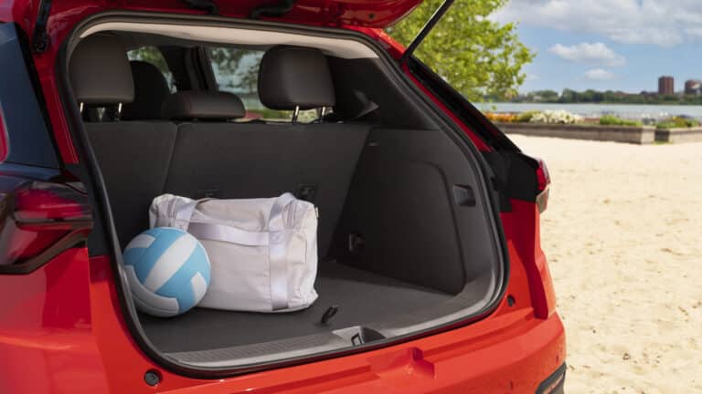 Open car trunk on a sandy beach with a white sports bag and volleyball inside.