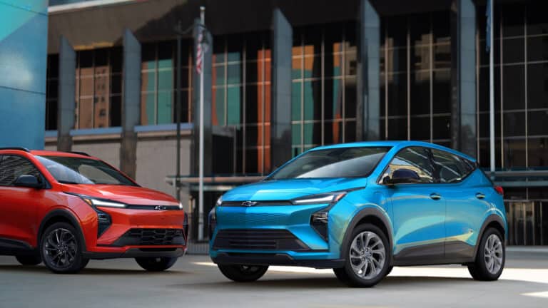Two electric SUVs, one red and one blue, parked in an urban setting against a modern building backdrop.