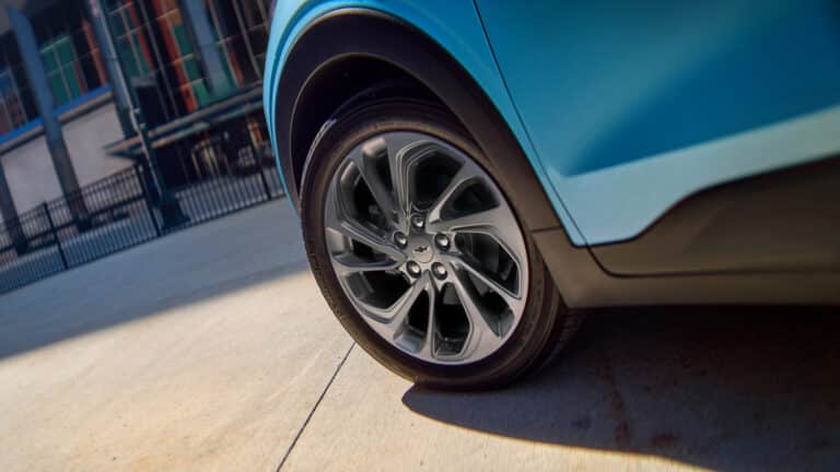 Close-up of a blue car wheel with stylish alloy rims on a concrete surface, city backdrop.