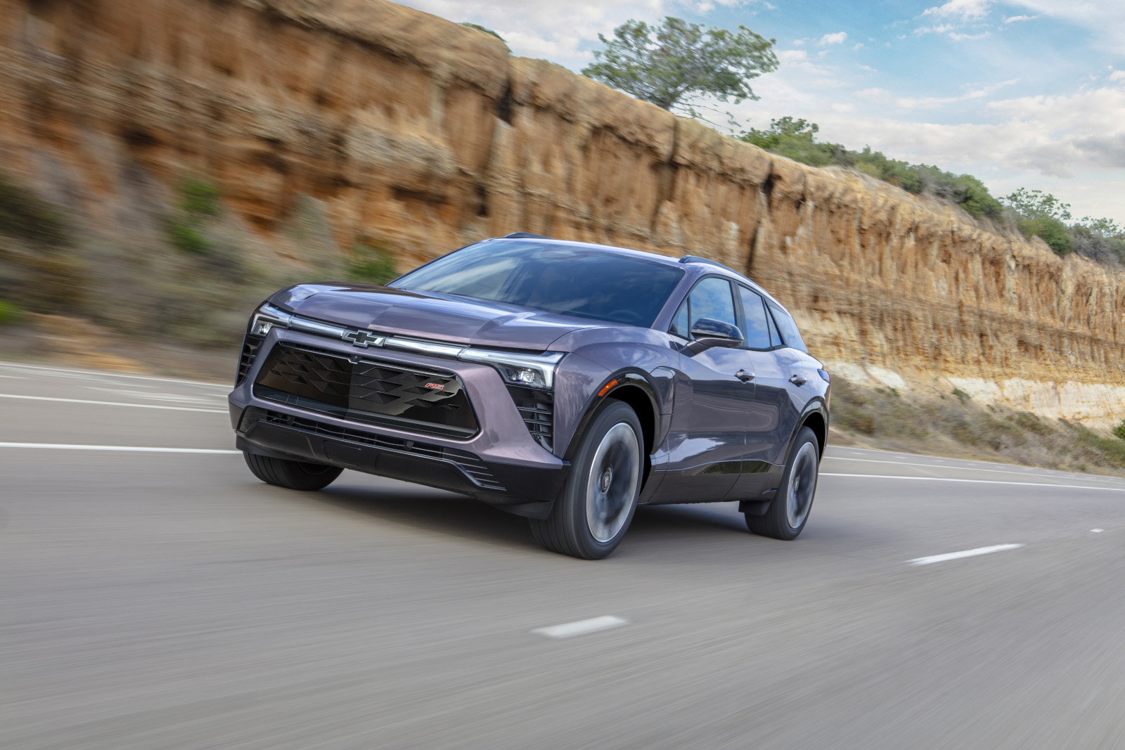 A sleek, modern SUV driving on a scenic highway with rocky cliffs in the background.
