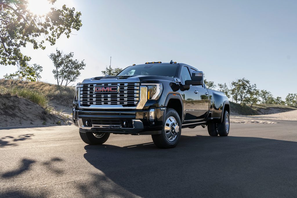 Black GMC truck parked on a sunlit road, surrounded by greenery and sand dunes.