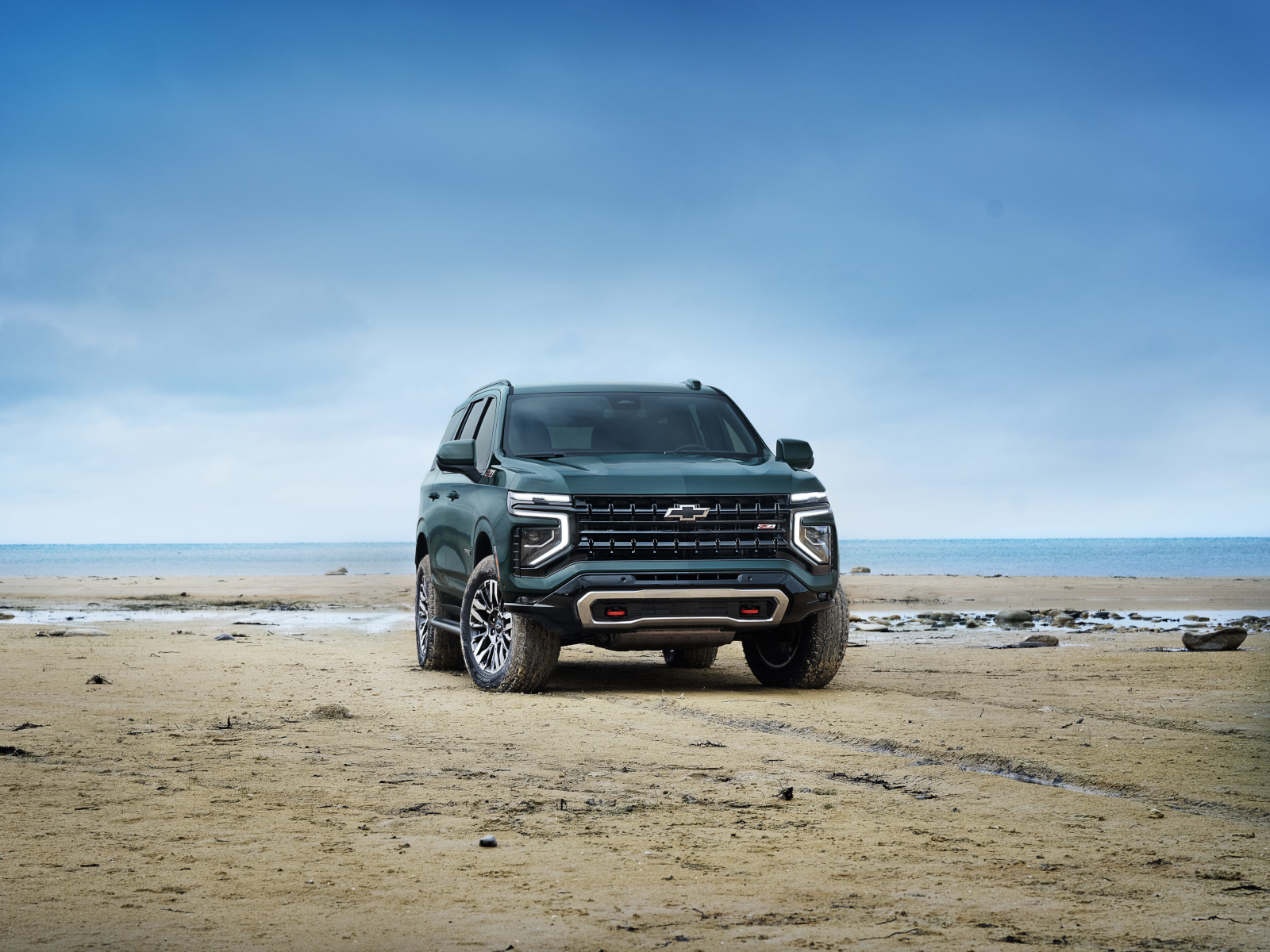 SUV parked on a sandy beach under a clear sky, with ocean in the background.
